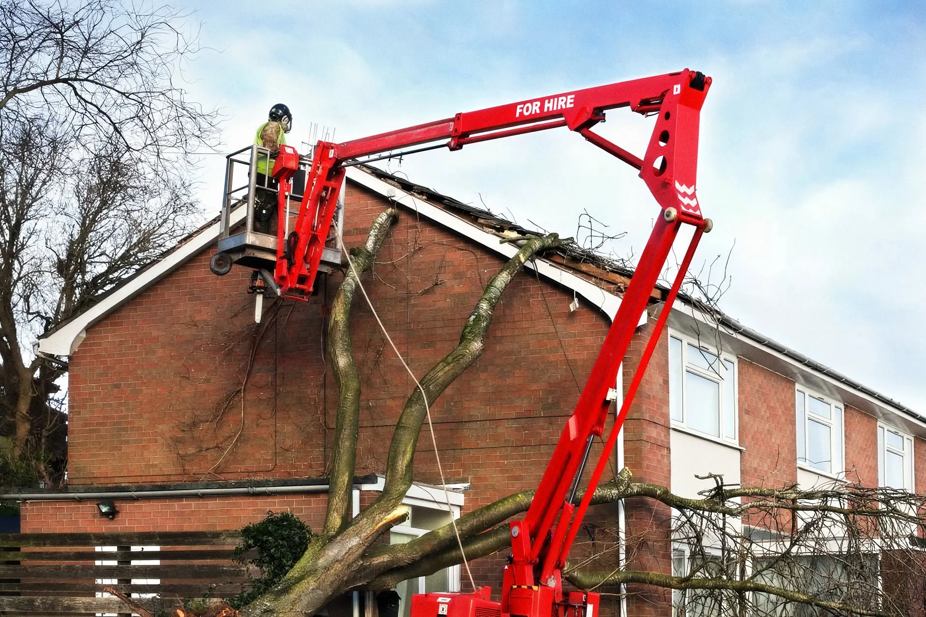 Crew working from a lift to remove storm-damaged tree limbs from a brick home